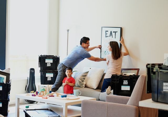 Two people hanging a painting up on the wall after moving into a rental with their kid