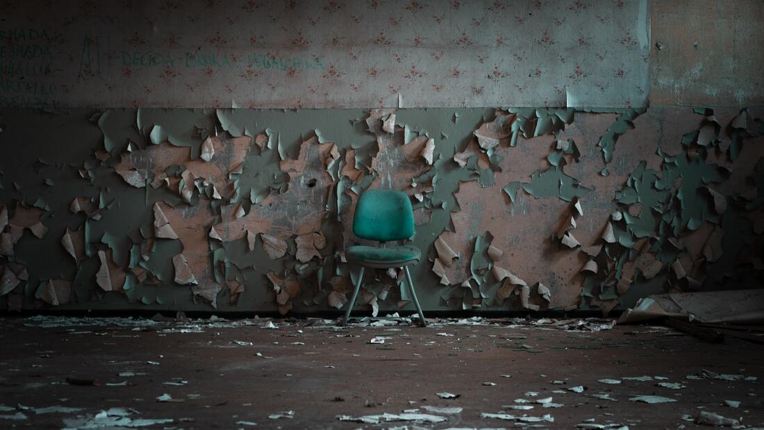 A worn-out chair lying against the wall in a damaged room