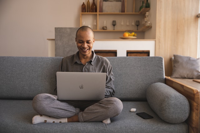 a man sitting on a couch in a living room, using a laptop